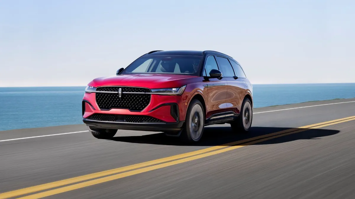 A red 2024 Lincoln Nautilus SUV driving on a road with a body of water in the background.
