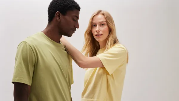 Two people pose in T-shirts in front of a light grey background.