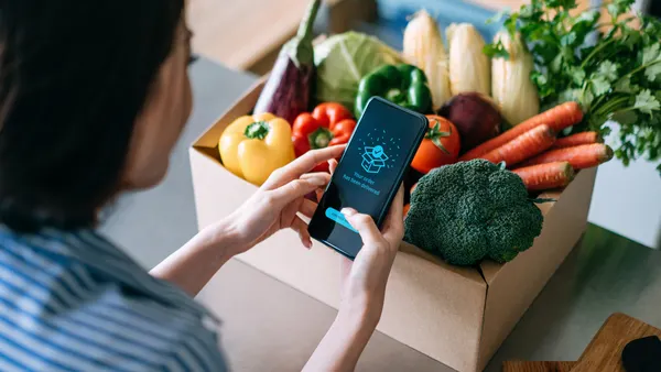 Woman with a vegetable box, looking at her phone with a delivery confirmation.