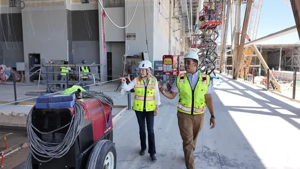 A man and woman in hardhats walk the site of a dusty construction project