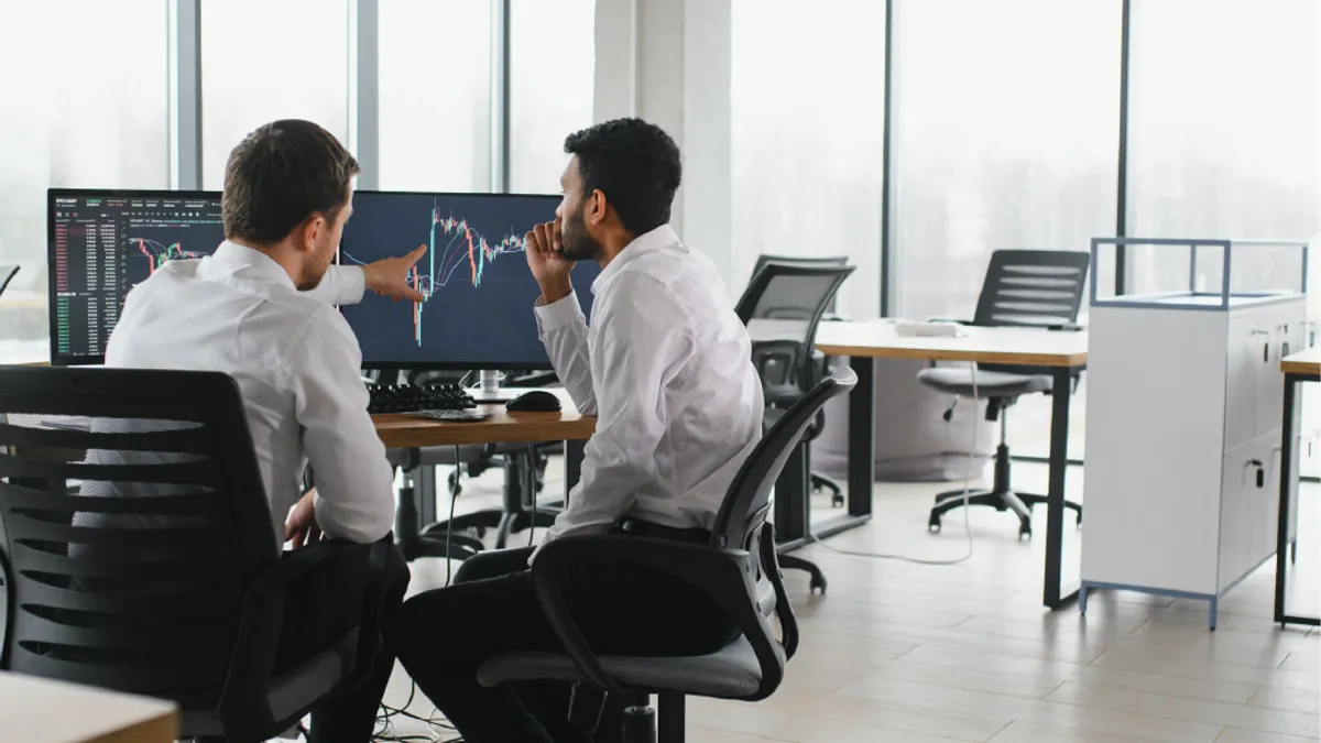 Two successful trader in formalwear pointing at display, analyzing stat and dynamic on forex charts, working in office together