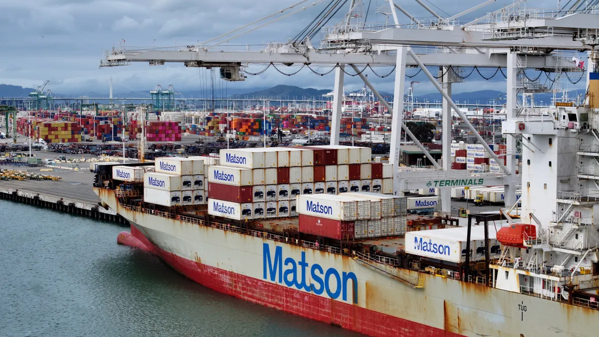 A ship labeled "Matson" carries several large boxes in front of a port.