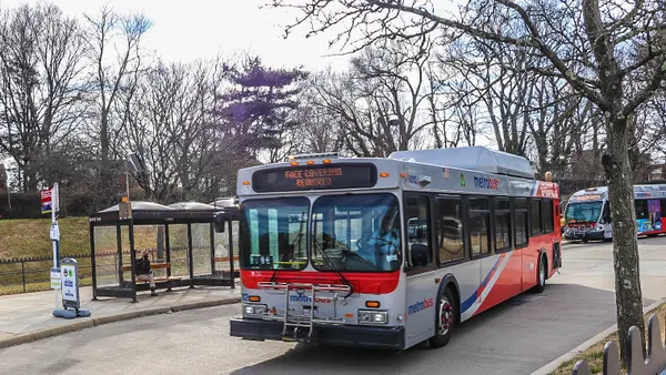 A Washington Metropolitan Area Transit Authority bus drives along a lane by a bus stop.