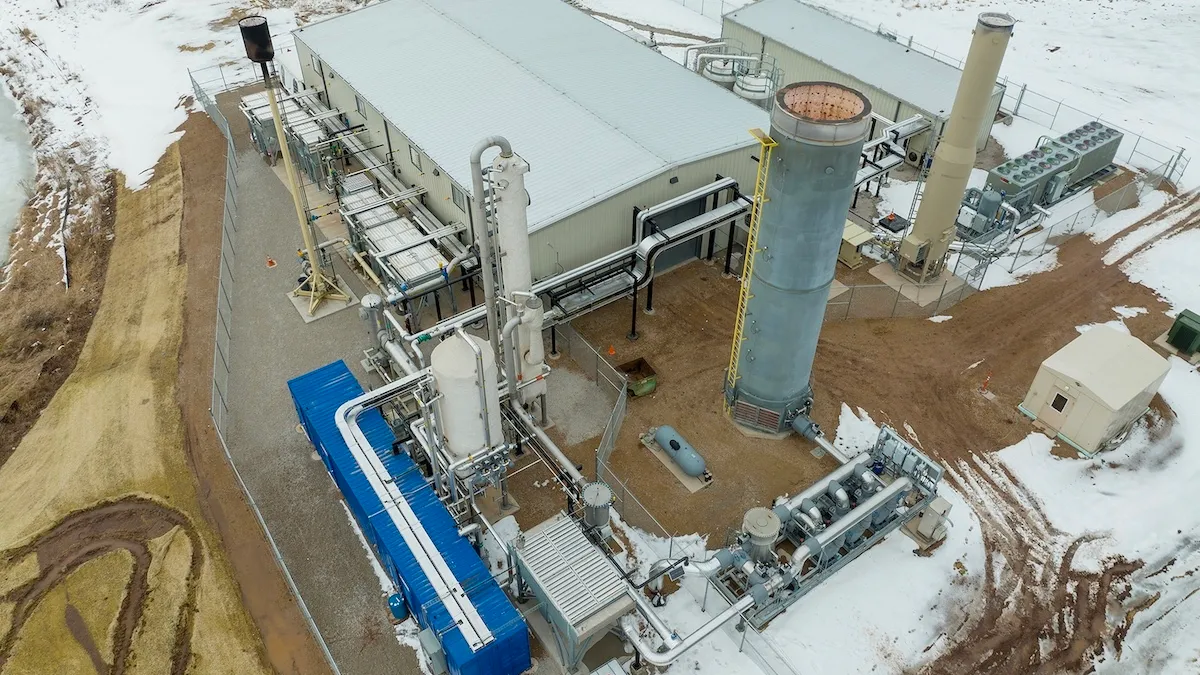 An industrial shed attached to several pipes and stacks in a snowy field.