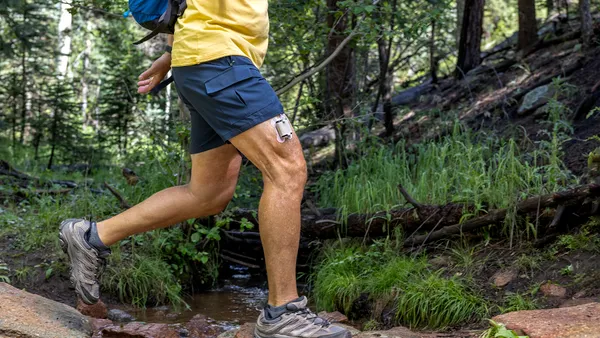 A person walks in a forest with a square device taped to their thigh.