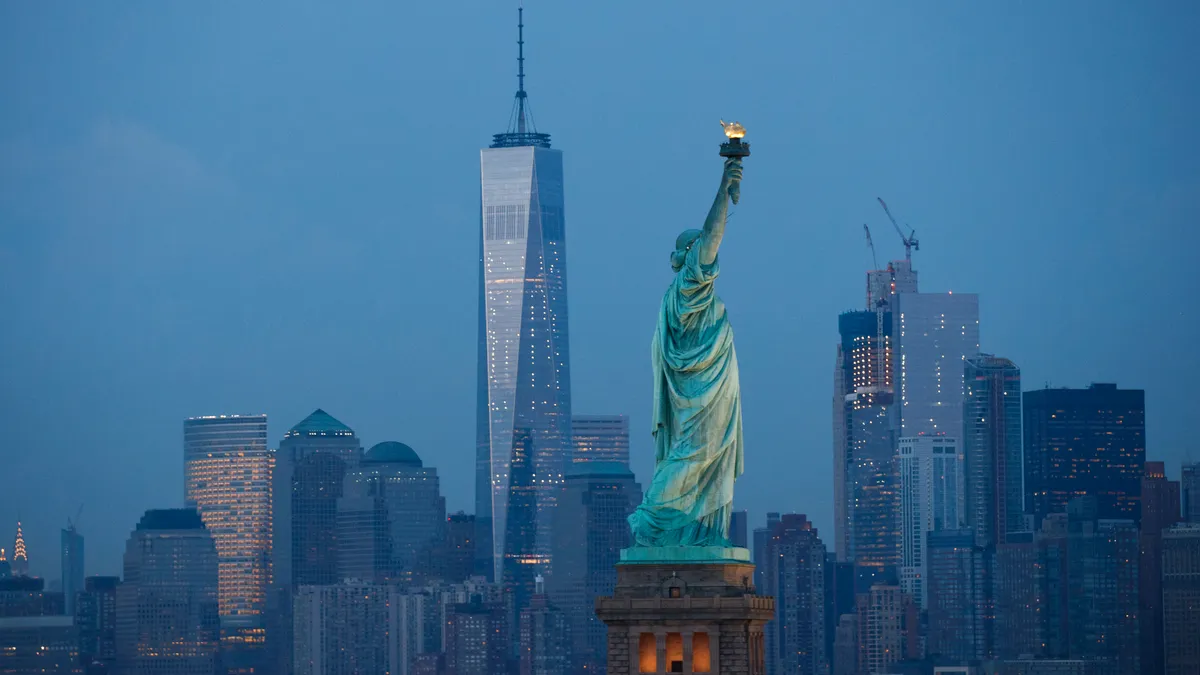 The Statue of Liberty from its right side at dusk, with New York's skyline as a backdrop.