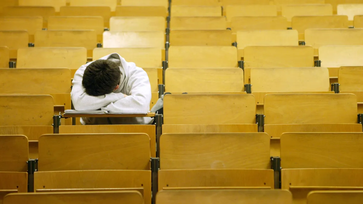 A student sits with their head down amid rows of empty desks.