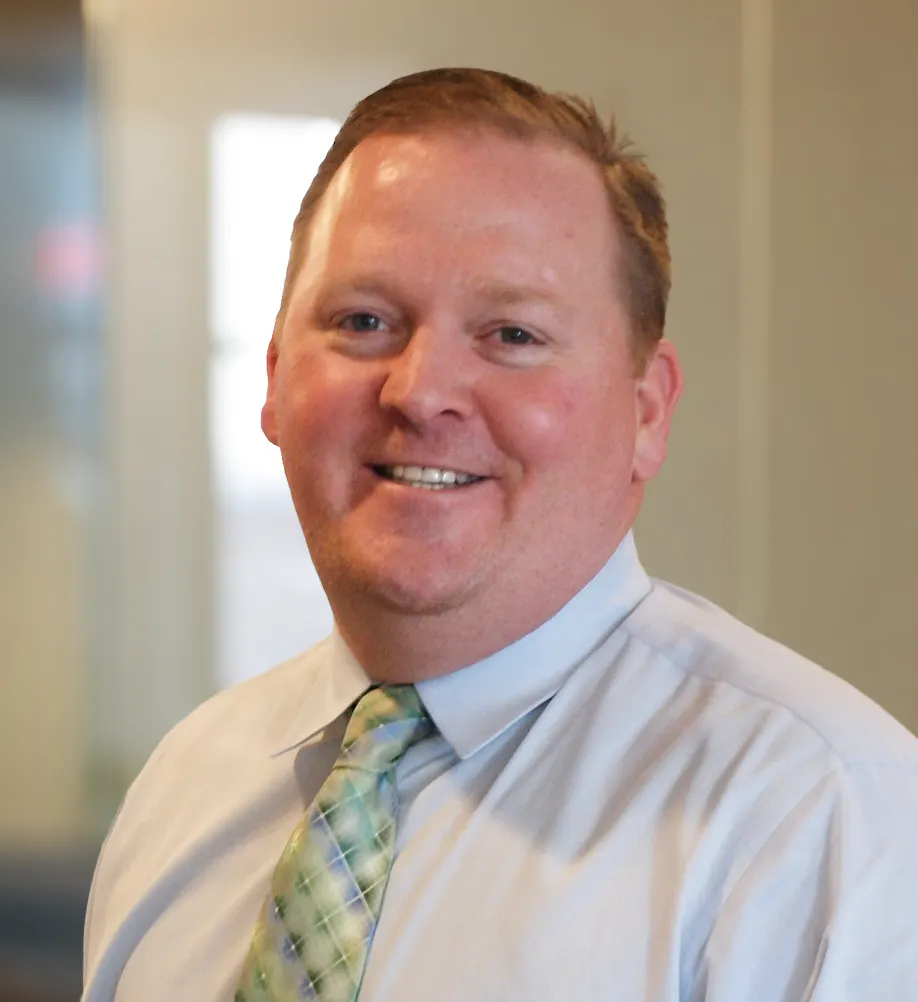 A headshot of a man with red hair wearing a shirt and tie.