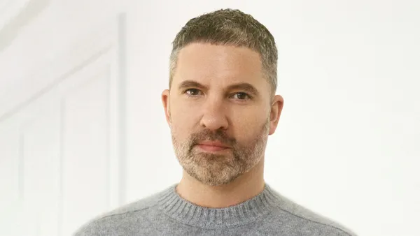 A corporate headshot features a man in a gray sweater and short cropped hair looking at the camera.