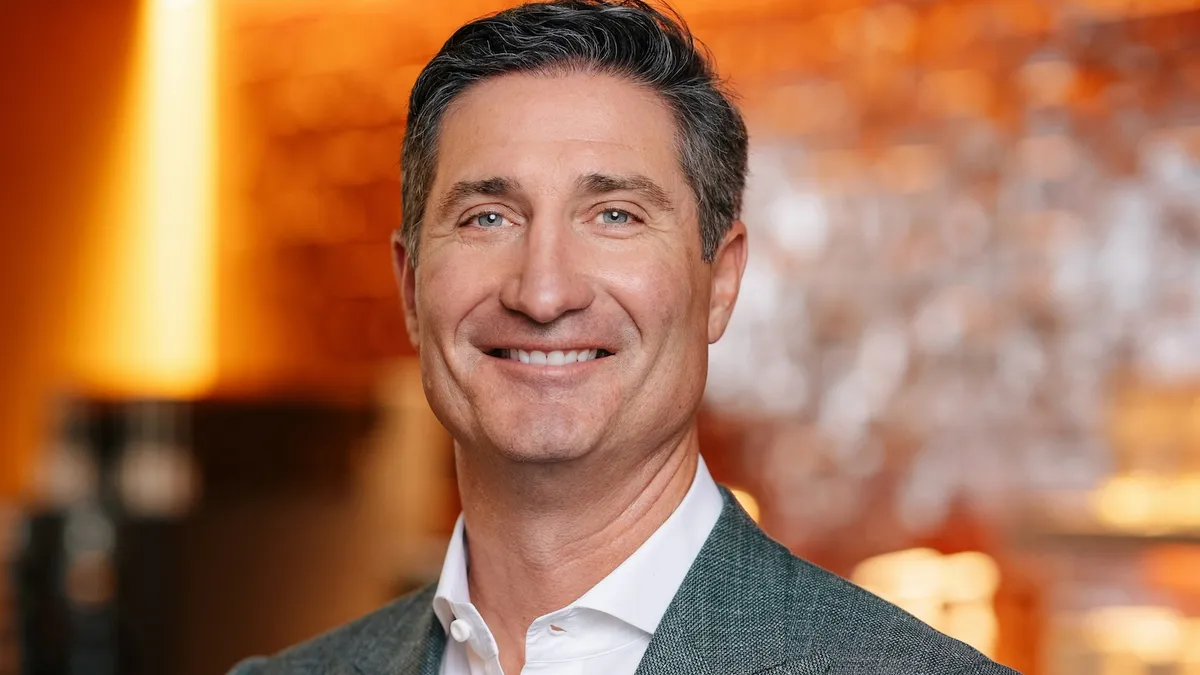 A smiling white man in a suit. He's wearing a jacket with peaked lapels and no tie, for what it's worth.