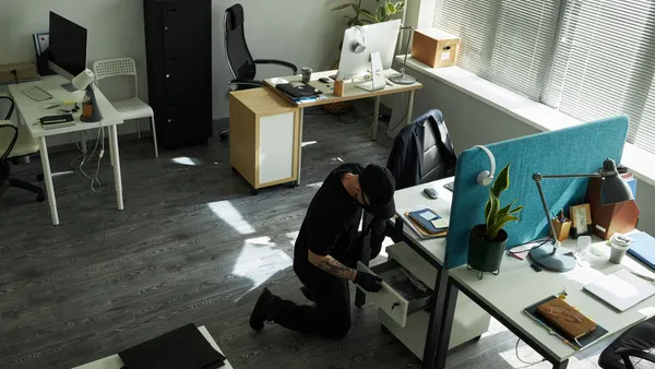 An intruder rummages through an office desk.