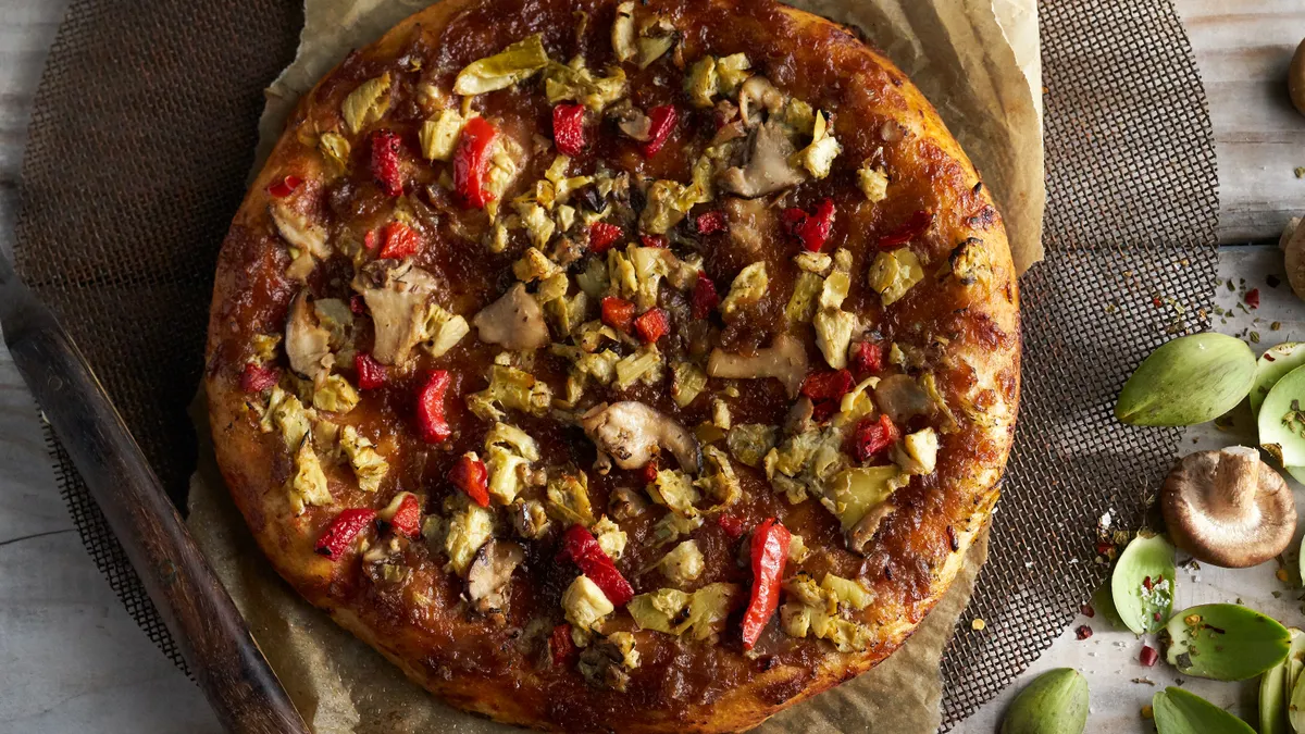 A roasted vegetable pizza sits on a wooden board