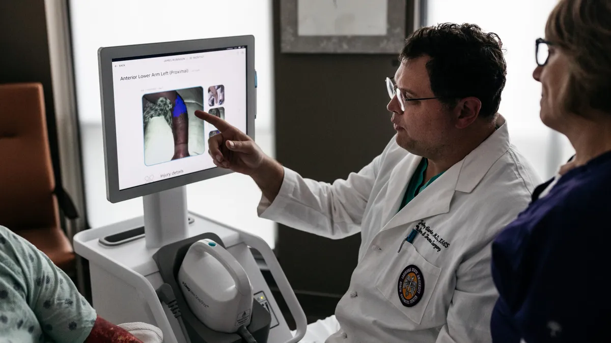 Two docotors in a hospital room looking at an image of a patient's burned arm.