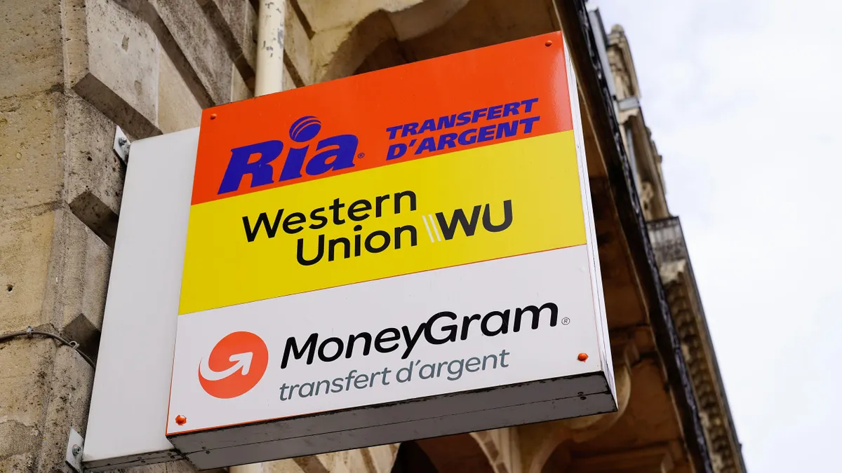 Exterior sign of a money transfer agency featuring logos for Ria, Western Union, and MoneyGram, mounted on a stone building in France.
