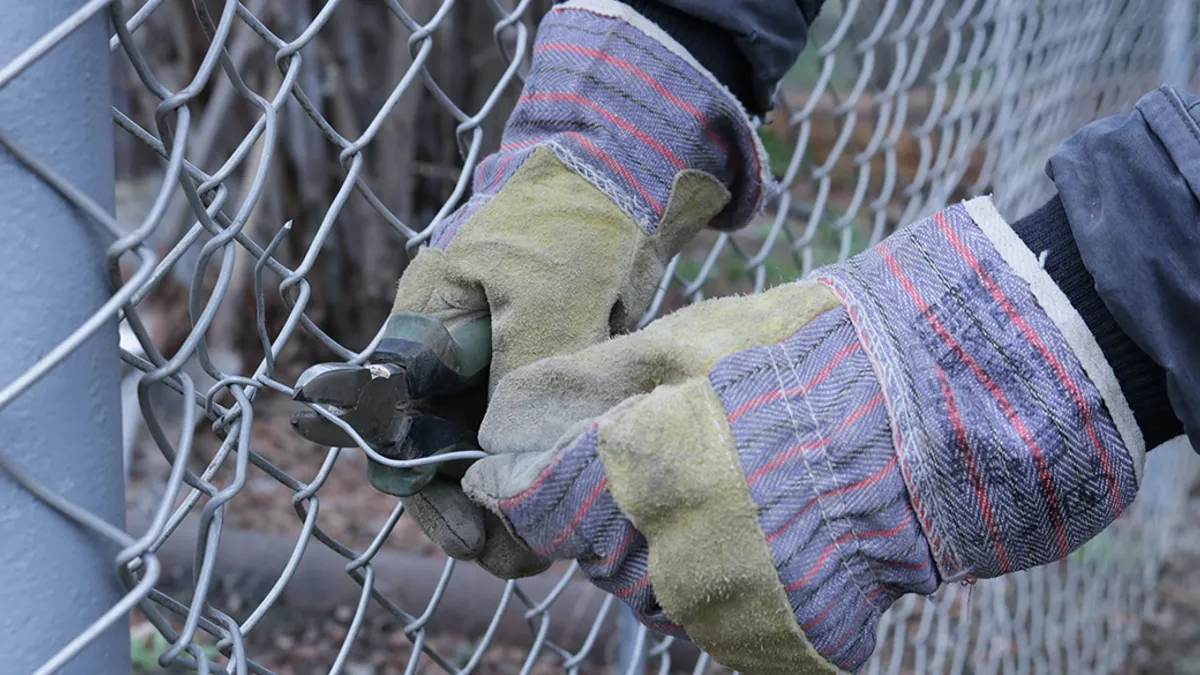 Gloved hands using pliers to clip chained fence