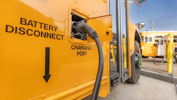 A yellow electric school bus is plugged in at a charging station.