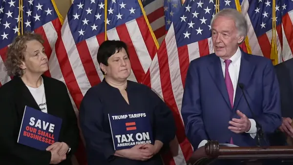 People gathered around a microphone, with U.S. flags behind them.