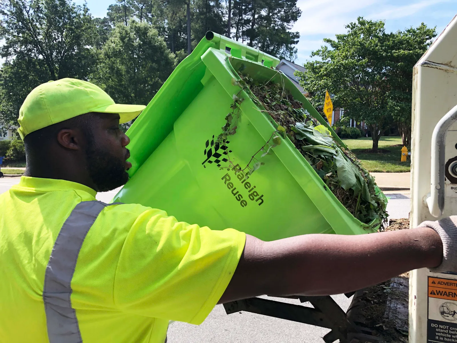 A yard waste collection worker empties a cart of yard waste into the back of a refuse truck.