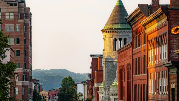 A street lined with historic brick buildings with forested hills in the background.