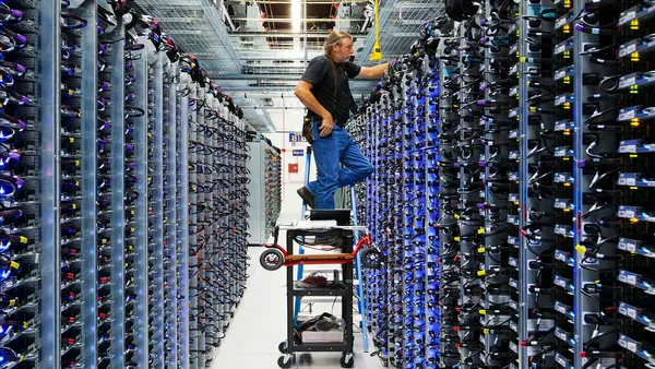 A man stands on a cart in an corridor between computer servers.