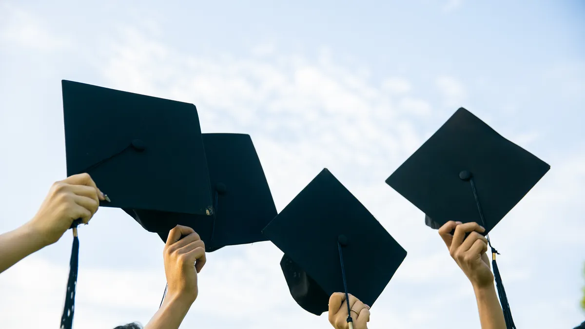 Four black graduation caps are being held up in the air by four hands.