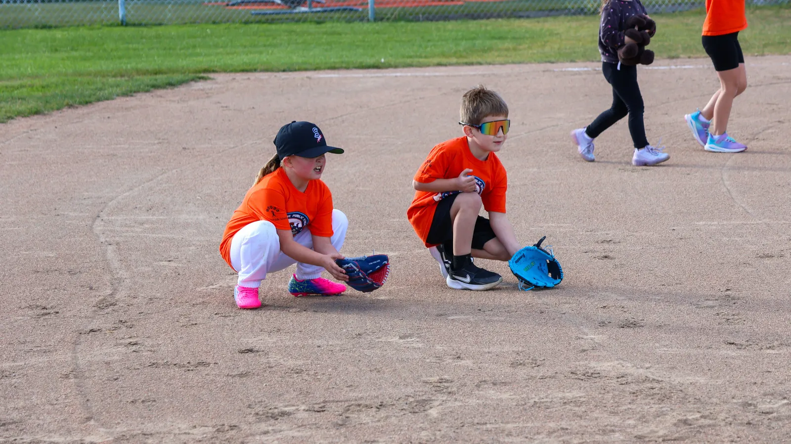 Two young children are playing T-ball on a baseball infield.