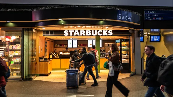 Customers with luggage walk by a Starbucks at an airport.