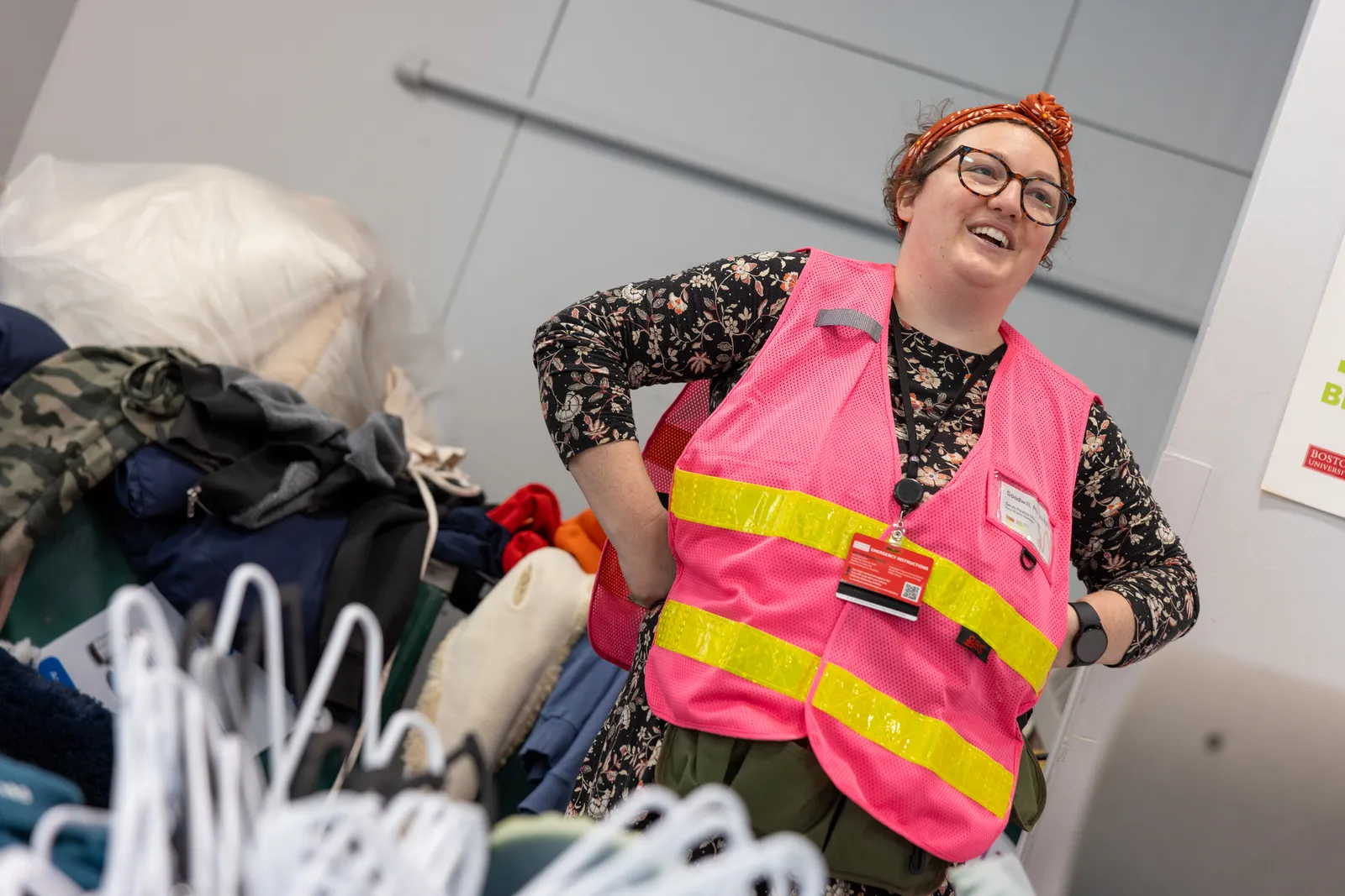 Sarah Healey of Boston University, wearing a safety vest and glasses, stands next to a pile of material for recycling and donation.