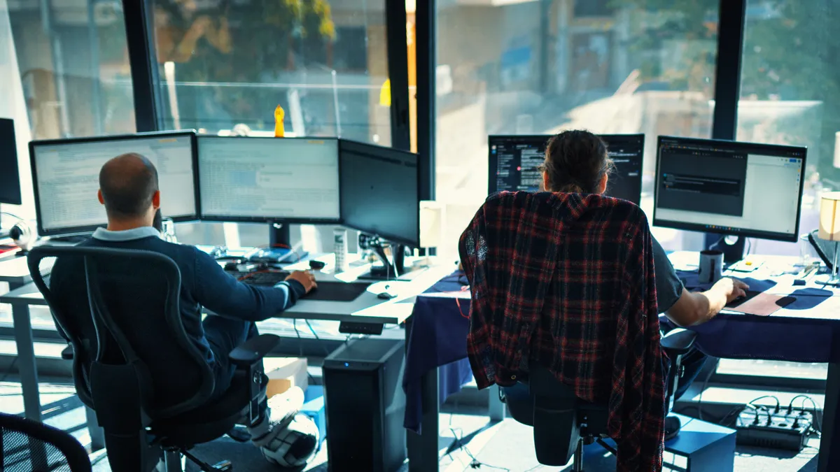 Closeup rear view of two people coding on multiple computers