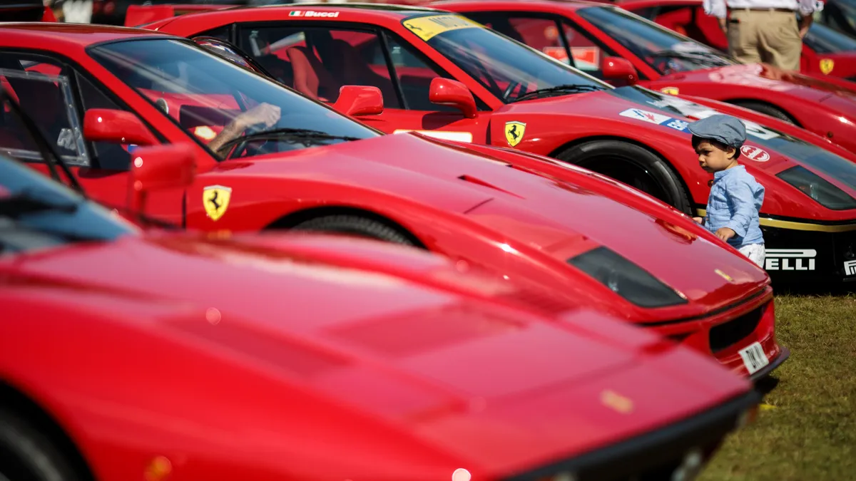 A child walks among a row of red Ferrari cars on display.