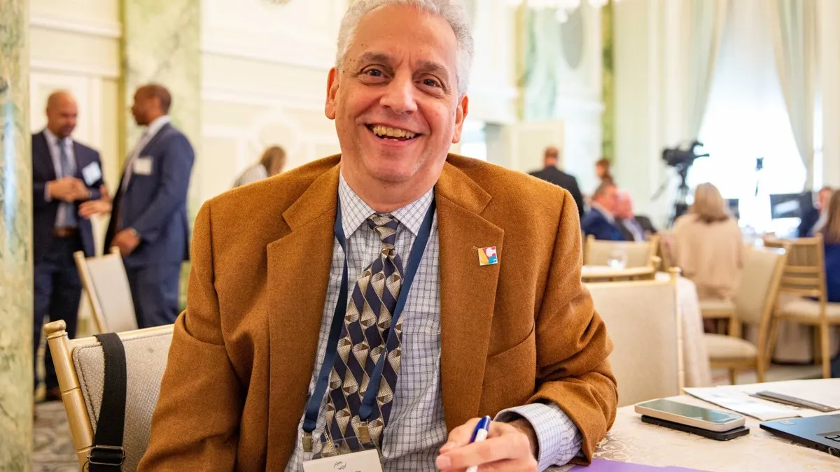 A man sitting at a conference table, smiles at the camera.