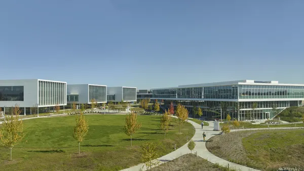 An exterior photo of a corporate campus shows flat buildings and a grassy lawn.