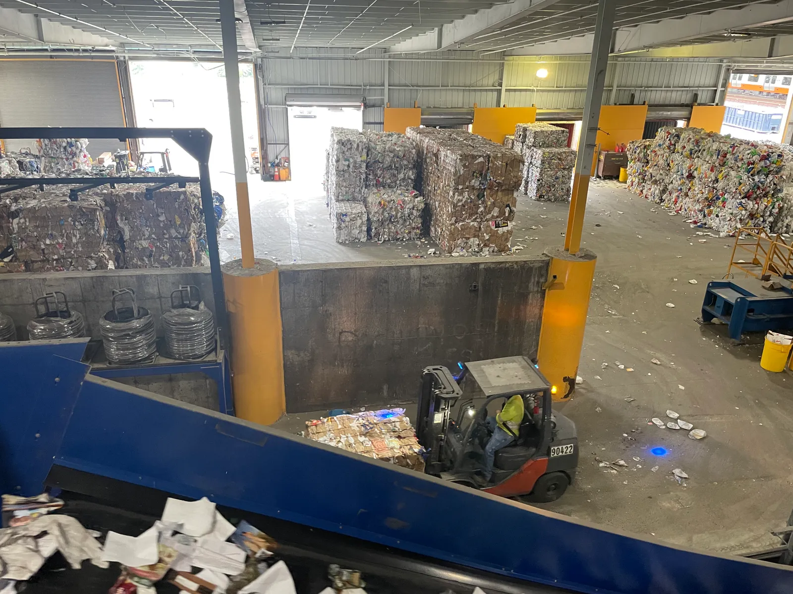 Person driving a forklift in a facility with bales of recycled materials