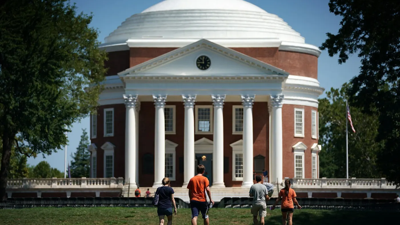 Four people in orange shirts in the middle ground walk away from the camera, against the backdrop of a large academic building with a white dome.