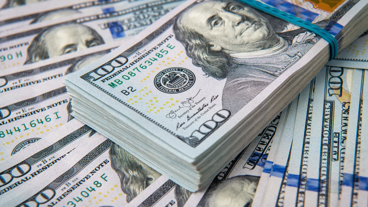 A close-up picture of a stack of one hundred dollar bills on top of fanned out one hundred dollar bills.