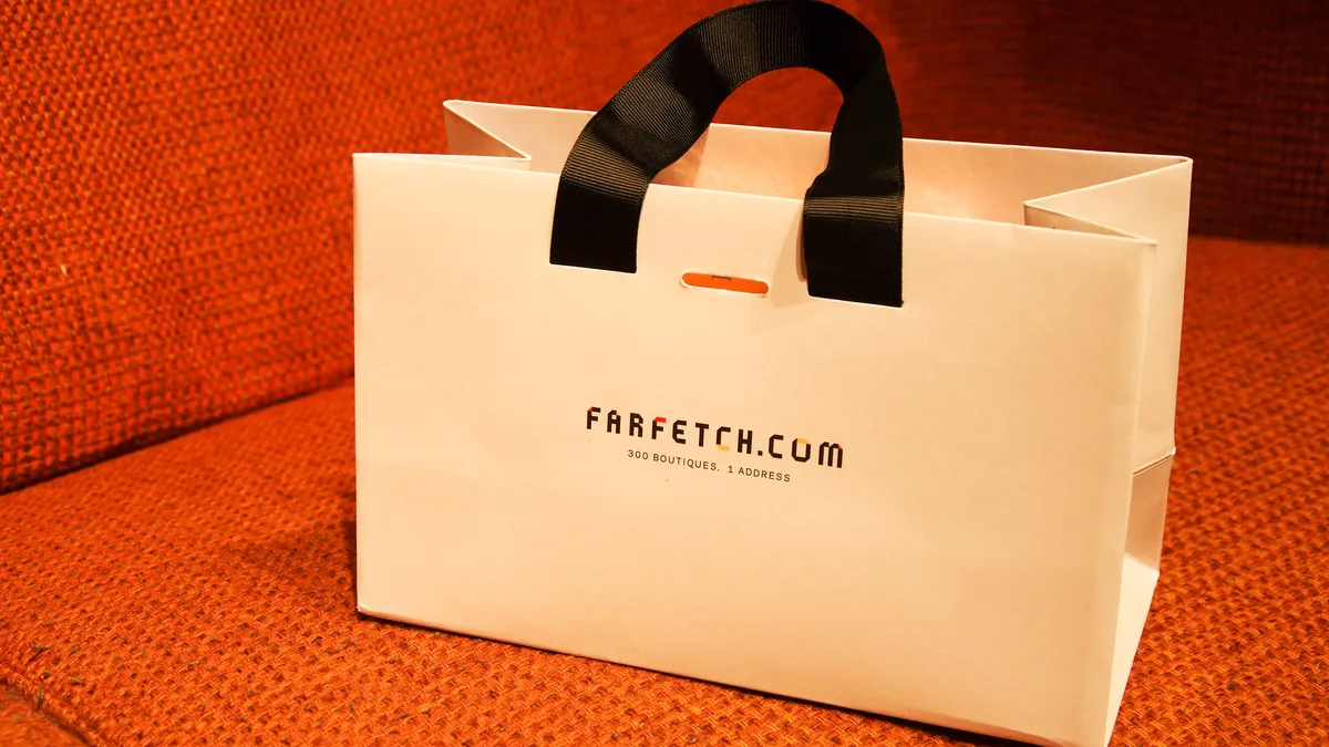 A Farfetch shopping bag sits on an orange seat.