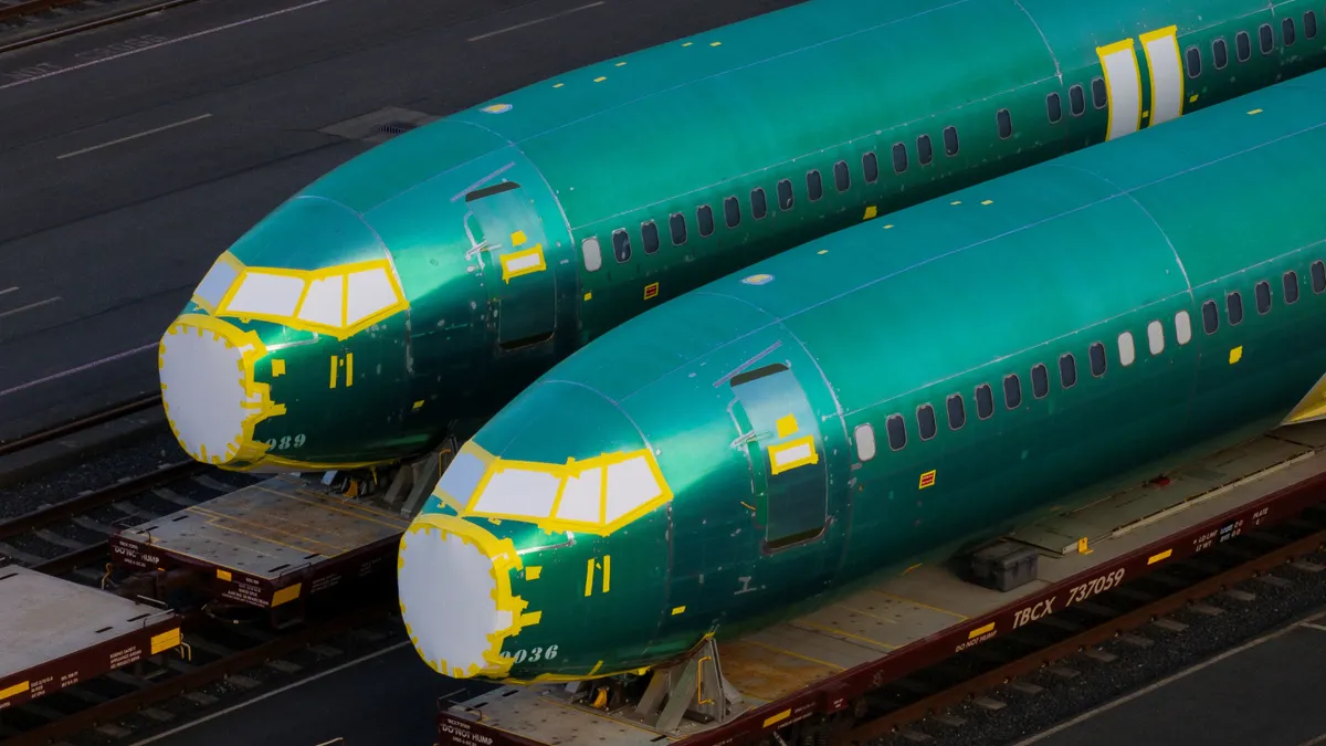 Two blue-greenish plane fuselages laying on rail cars side by side.