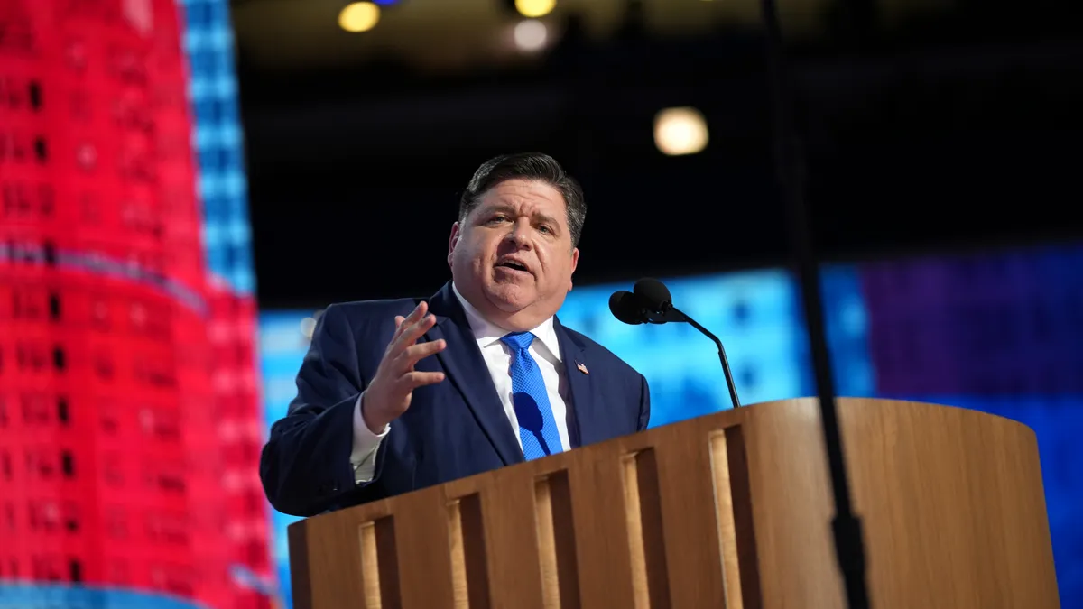 Illinois Gov. J.B. Pritzker speaks into a microphone behind a wooden podium on stage at the Democratic National Convention at the United Center on August 20, 2024 in Chicago, Illinois