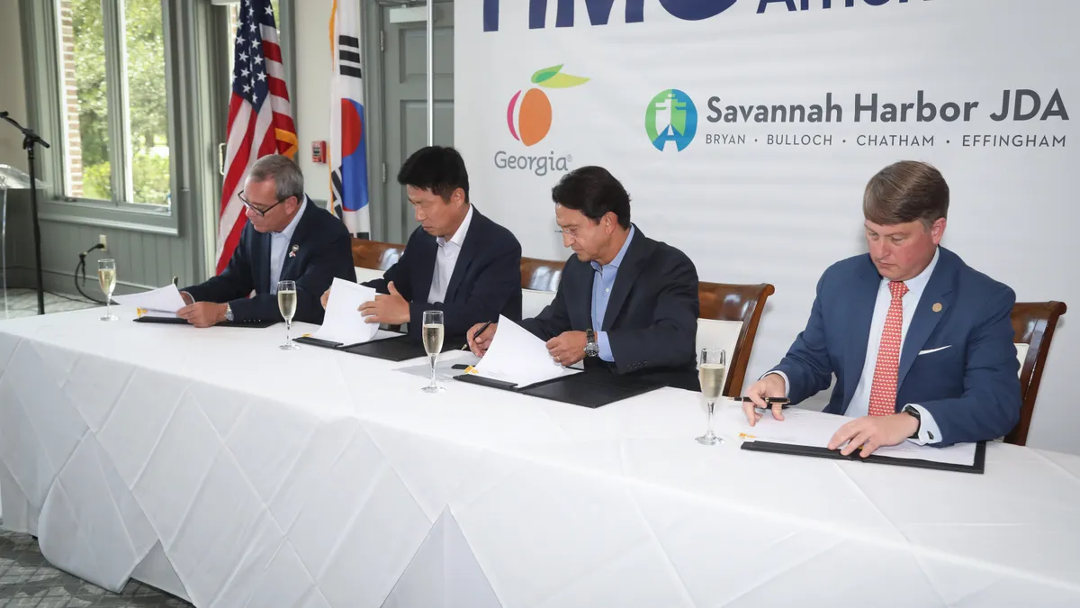 Four people sitting at a table signing documents and a glass of wine in front of them.