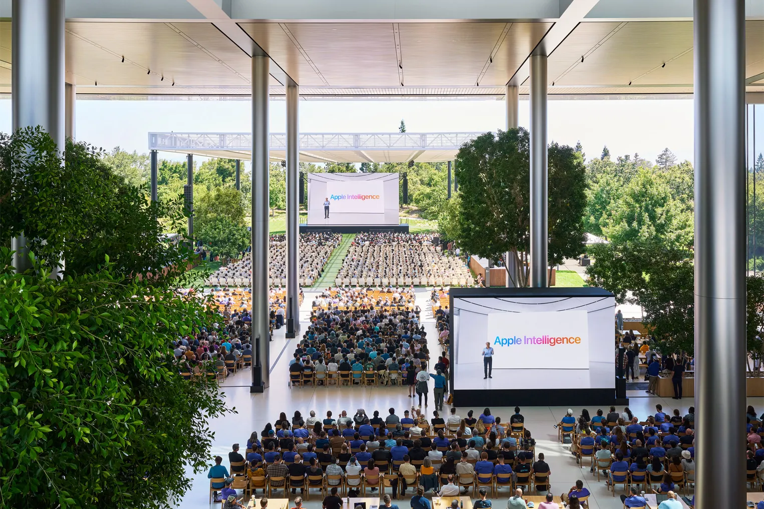 Apple WWDC 2024 attendees sit in chairs in front of a dias and two screens showing the words "Apple Intelligence."