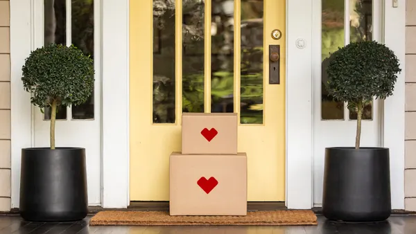 Two corrugated boxes with red heart symbols on the front are stacked on a doorstep.