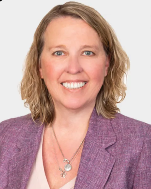 Woman with shoulder length blond hair wearing a purple blazer smiles.