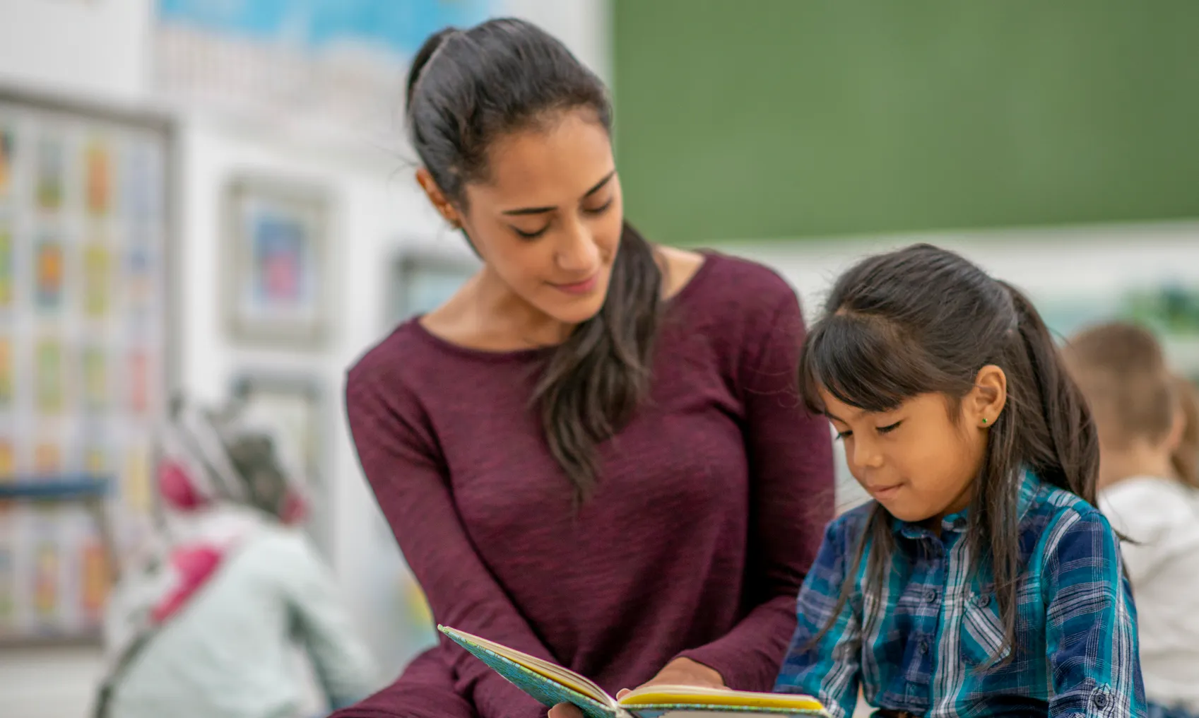 A woman teacher instructs a girl elementary student in reading.