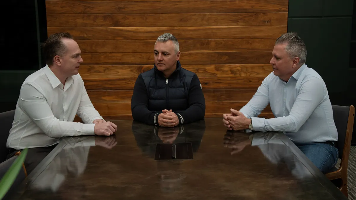 Three men sit at a boardroom table