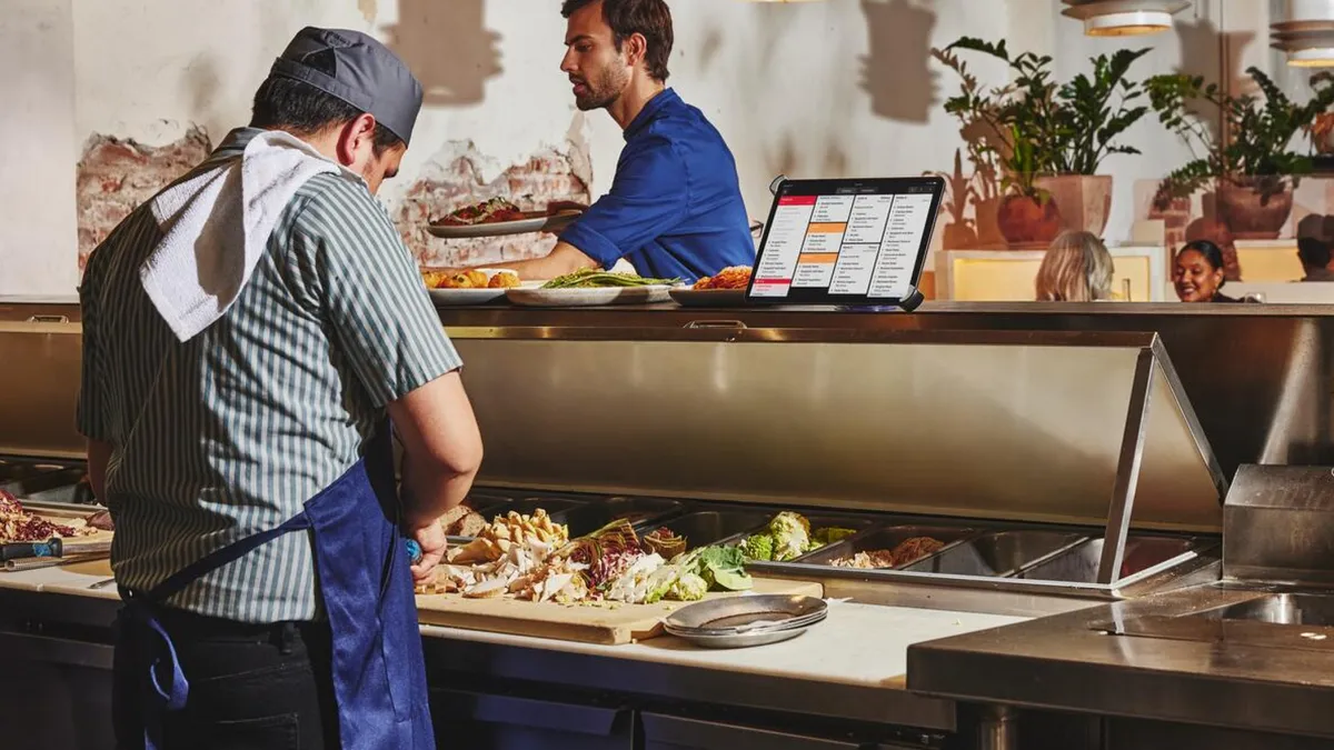 A cook prepares food on a preparation line while a mobile device is attached at the top of the line.