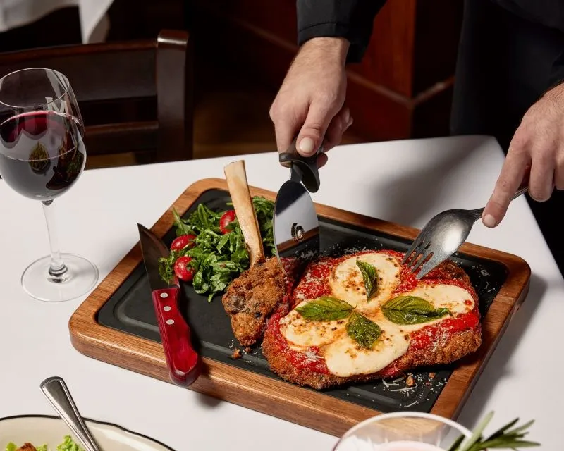 An arm from a server cuts a veal parmasan dish.