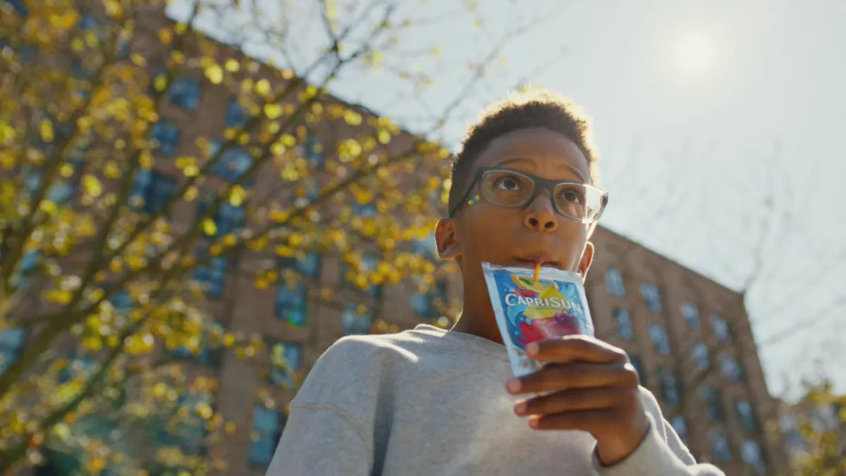 A kid drinks a Capri Sun outside during the day