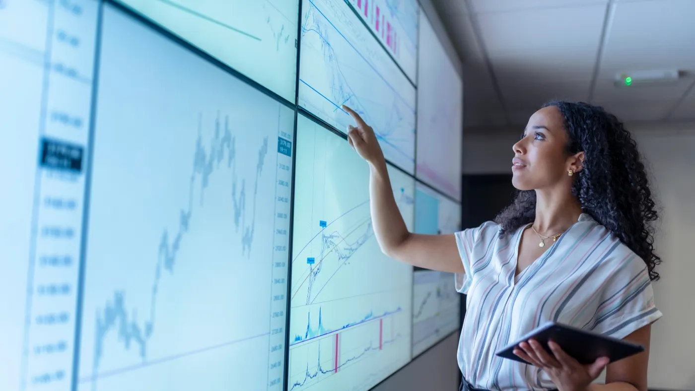 Professional with tablet pointing at charts on interactive screens