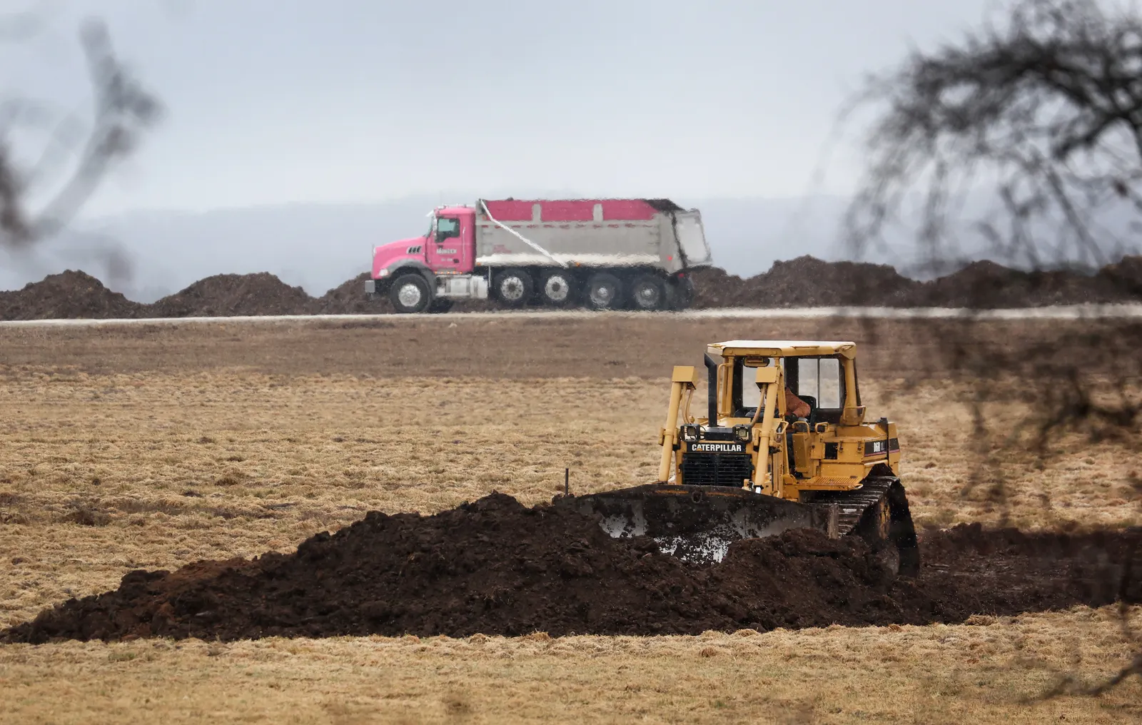A piece of heavy equipment prepares land for disposal of animal carcasses, with a truck in the background