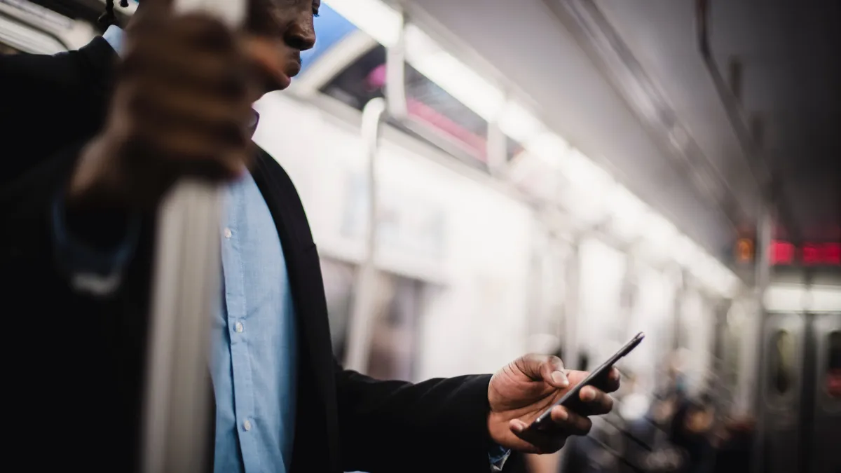 (Out of focus) A mid-30s Black person with dreadlocks looks at their phone on the underground subway